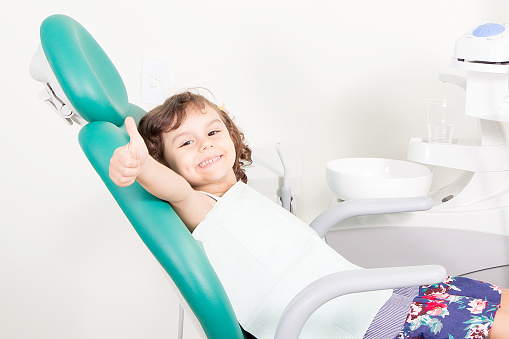 a smiling child in the dental chair giving a thumbs up