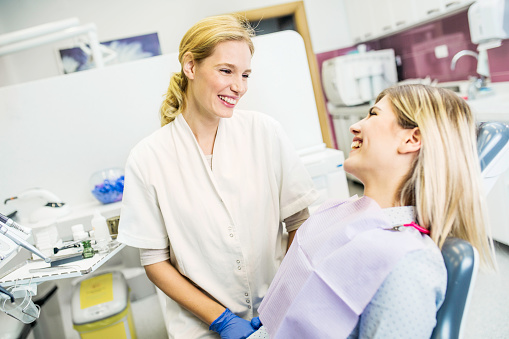  female dental professional and female patient in dental chair talking and smiling