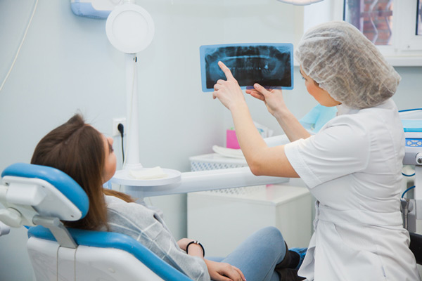 patient lying in dental chair and looking at a montior displaying a digital x ray while a dental professional points to the area in question