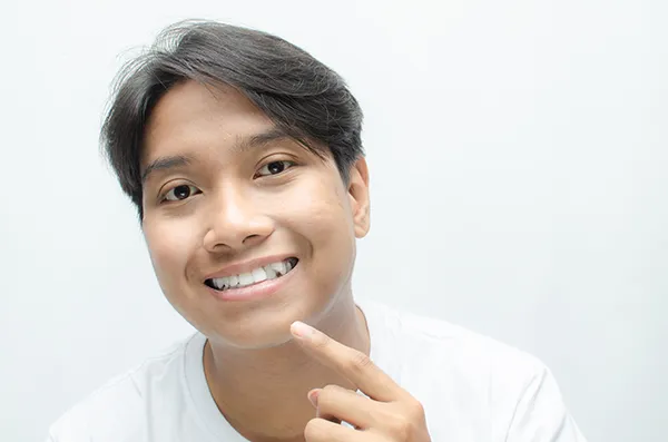 A partially smiling man points to his crooked upper teeth, indicating his eagerness to receive orthodontic treatment.