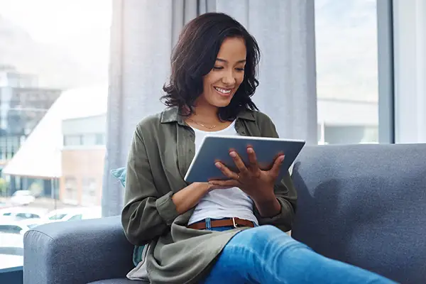 A woman smiling and sitting on a sofa while reading a dental blog article, while sitting on a sofa.