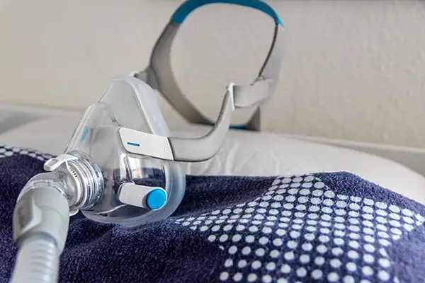 Close-up of a CPAP mask placed on a bed, showcasing sleep apnea technology used to improved breathing.