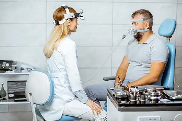 Female doctor speaks with a male patient about sleep apnea treatment options while he wears a CPAP sleep apnea machine.